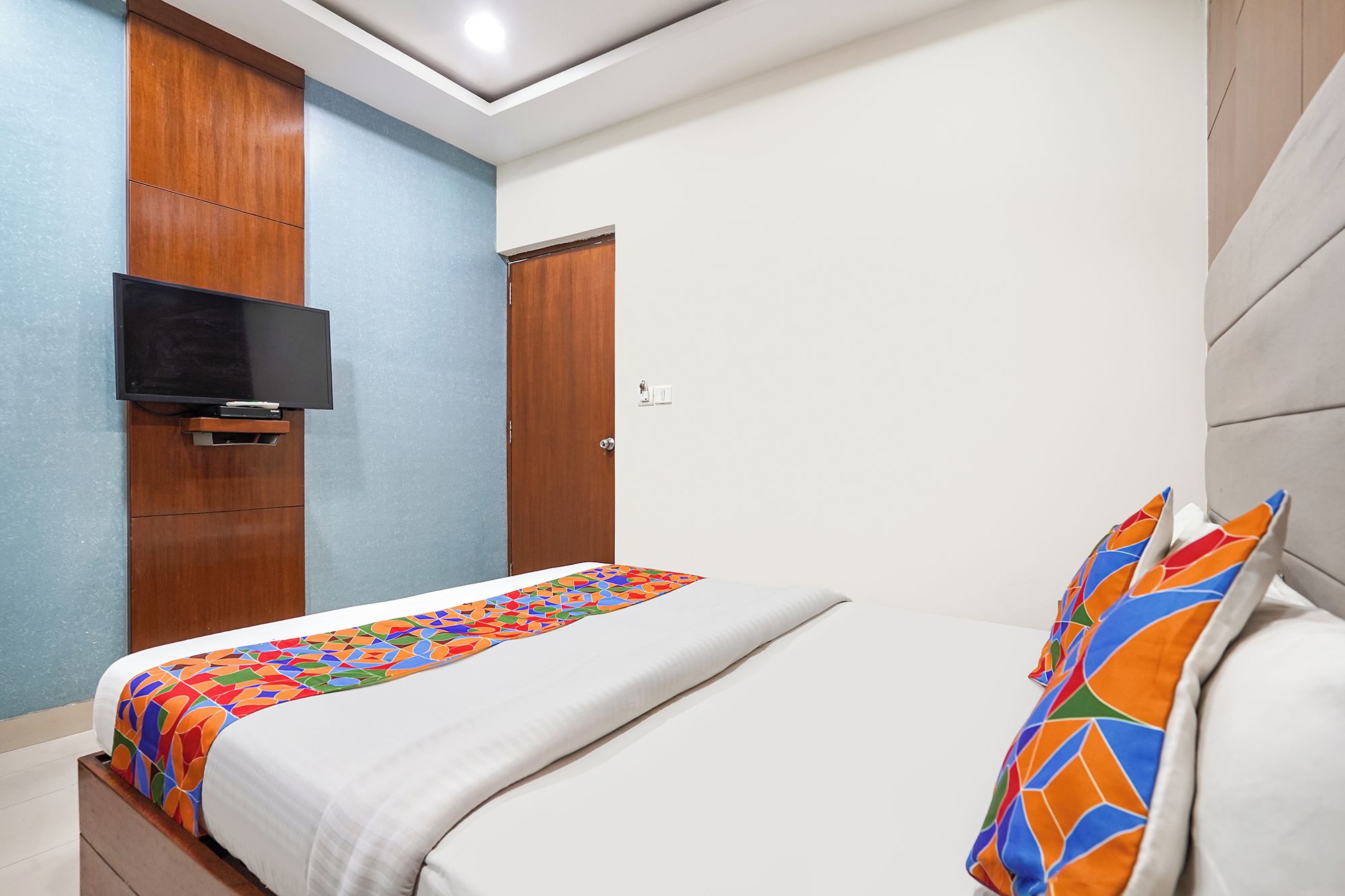 Una habitación de hotel con una cama, un televisor montado en la pared y una puerta.