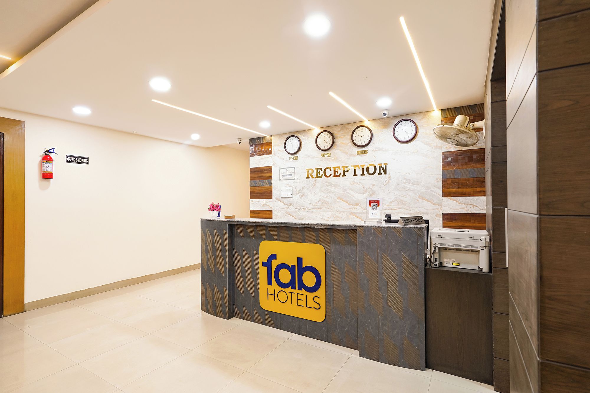 A hotel reception area with a reception desk, a 'No Smoking' sign, clocks, and a 'Reception' sign.
