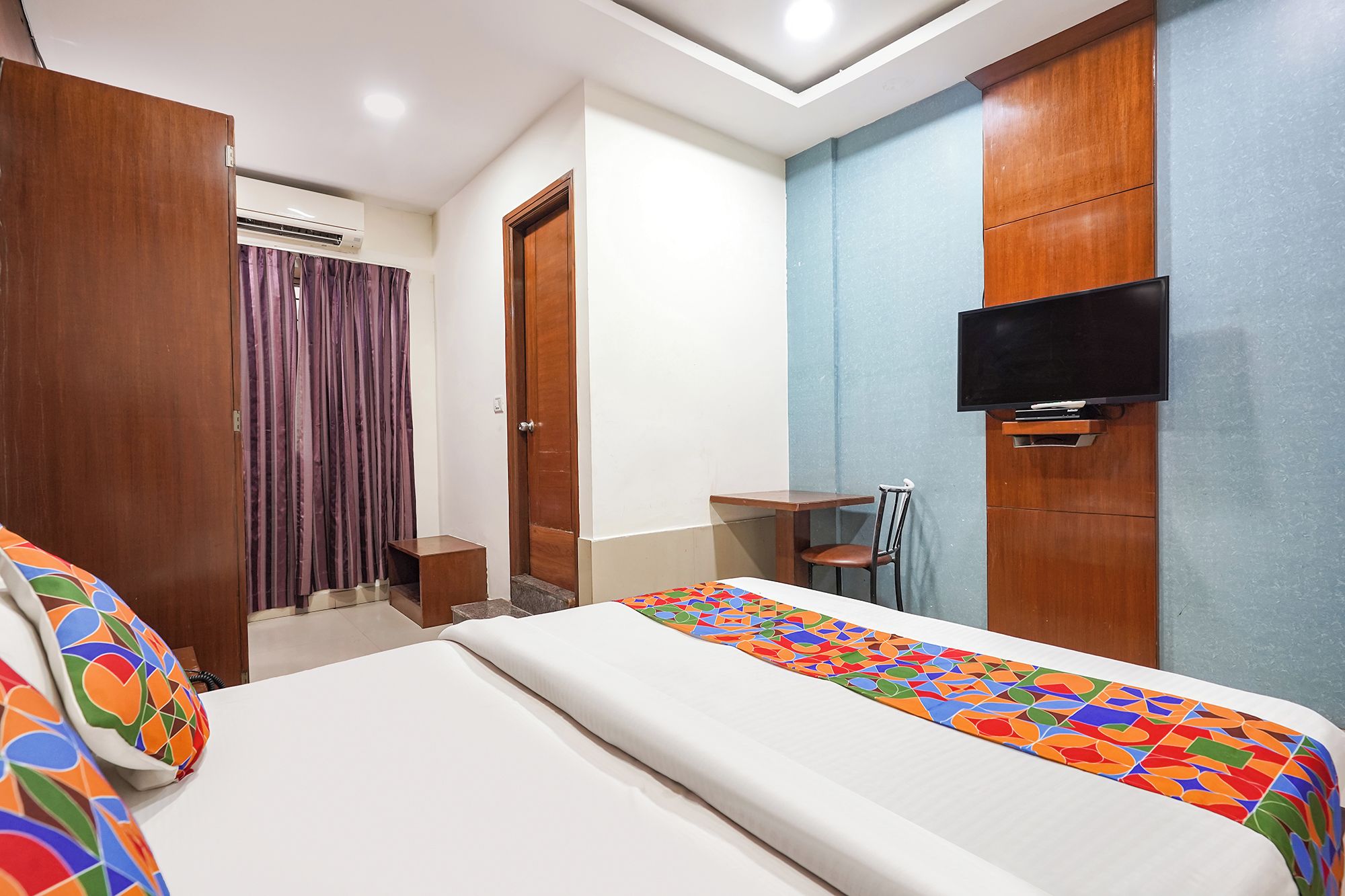 A hotel room with a bed, a television mounted on the wall, and a small table with a chair.