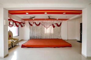 A room with a large bed, a ceiling fan, and a red and white curtain backdrop. - FabHotel Rama Palace (Nashik)