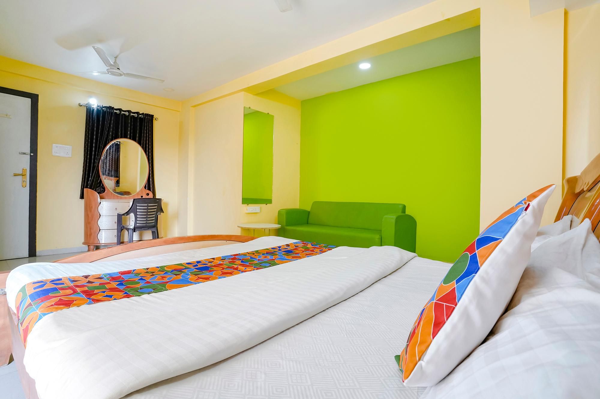 A hotel room with a bed, a green sofa, a small table, and a mirror.