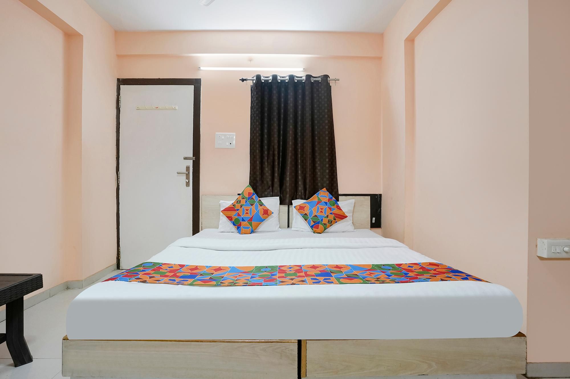 Un dormitorio con una cama, dos almohadas, una cortina, una puerta y una mesita de noche.