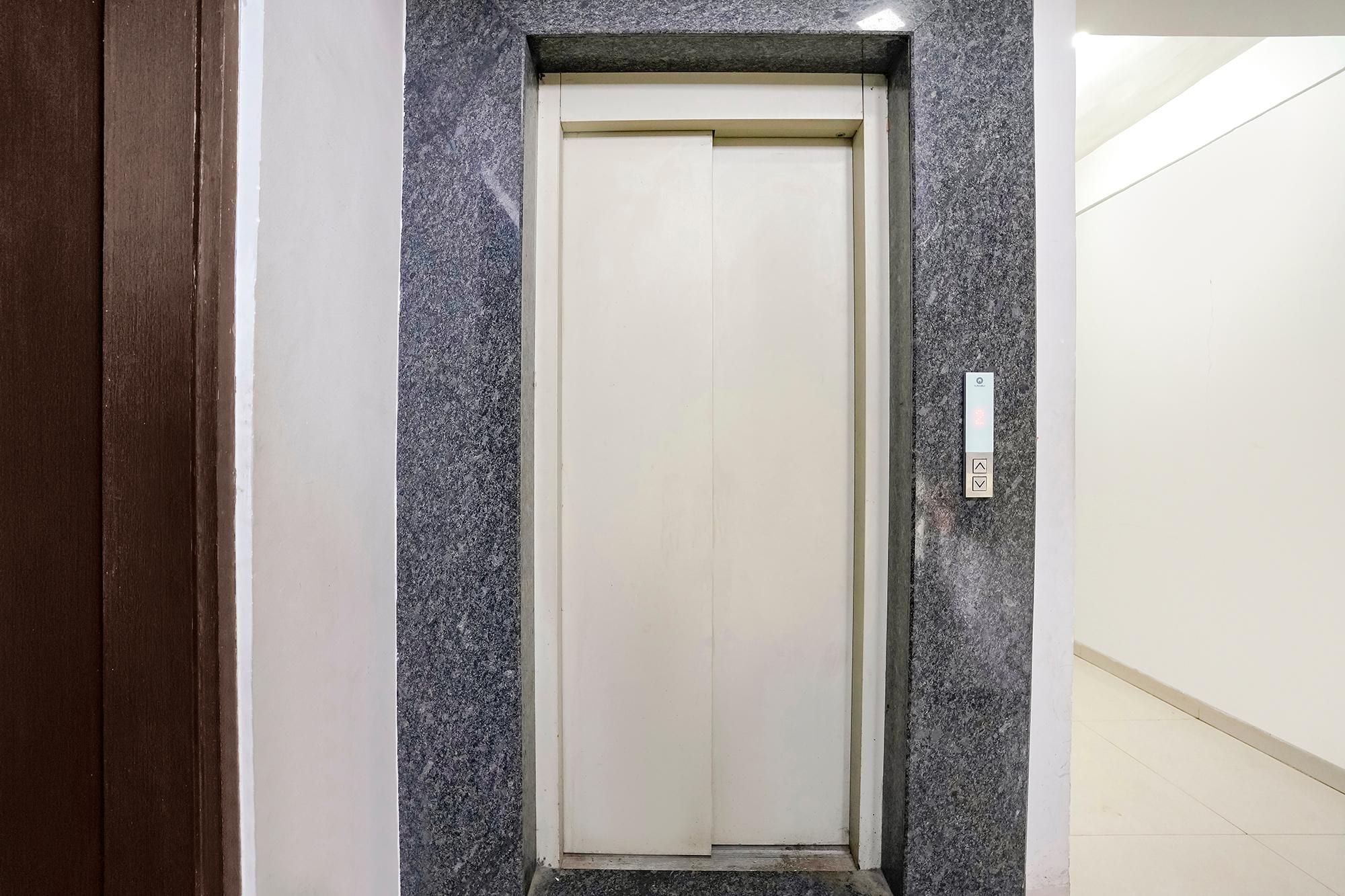 A closed elevator door with a marble wall and a light switch on the wall to the right.