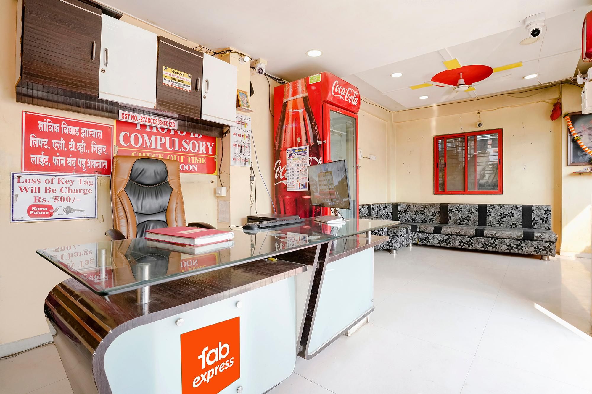 Zona de recepción de un hotel con un mostrador de cristal, una máquina expendedora roja de Coca-Cola, un sofá y un calendario colgado en la pared.