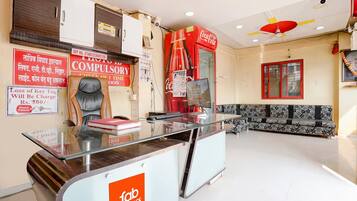 Zona de recepción de un hotel con un mostrador de cristal, una máquina expendedora roja de Coca-Cola, un sofá y un calendario colgado en la pared.