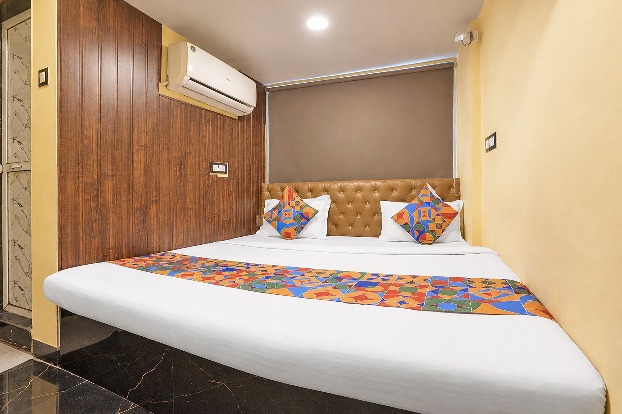 Una habitación de hotel con cama, armario de madera, unidad de aire acondicionado y lámpara de pared.