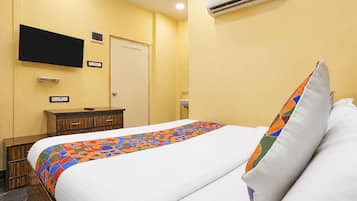 Una habitación de hotel con una cama, un televisor montado en la pared, una mesita de noche y un aire acondicionado.