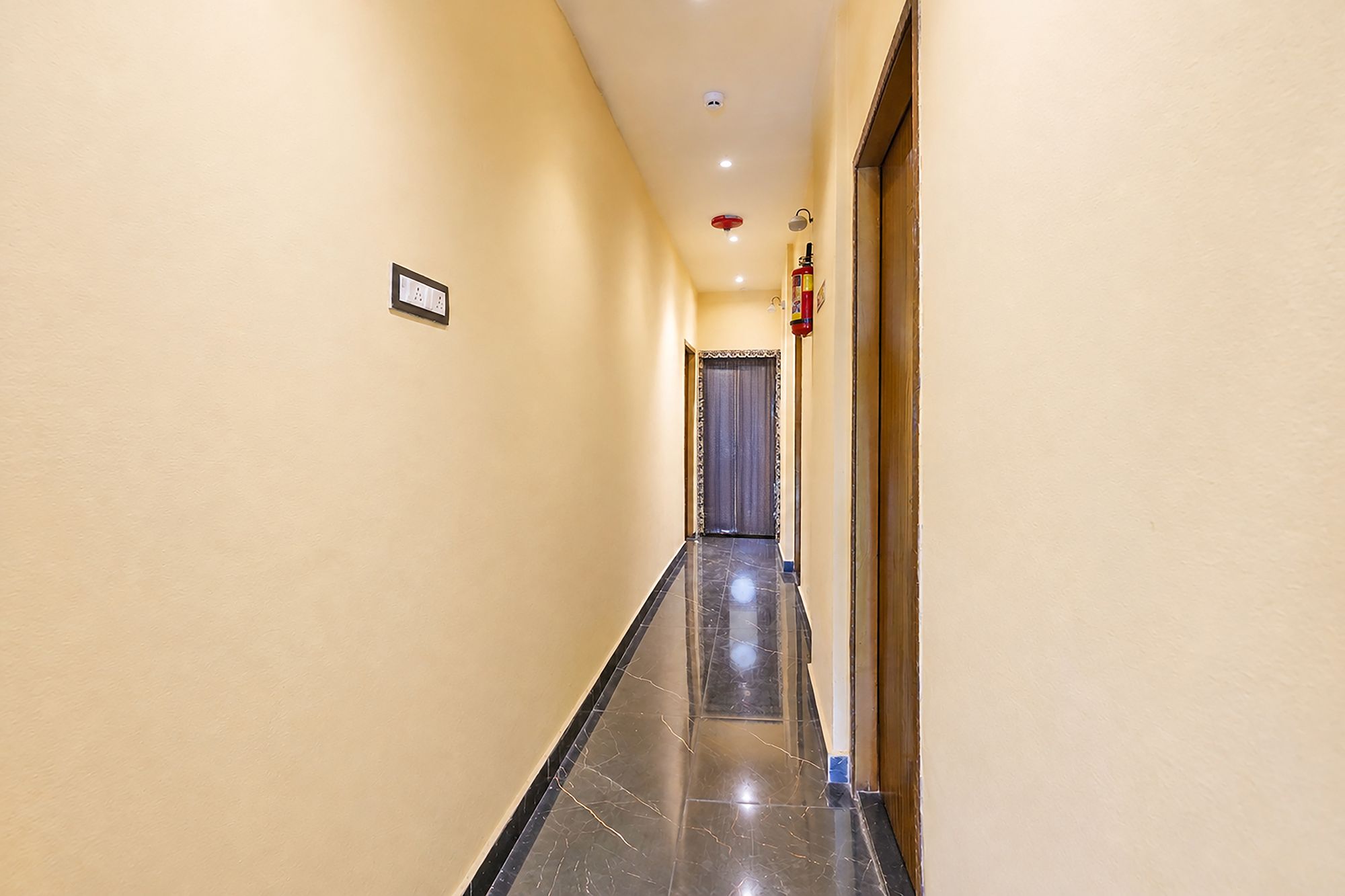 Un pasillo con piso de mármol, una puerta al final y un extintor de incendios fijado en la pared.