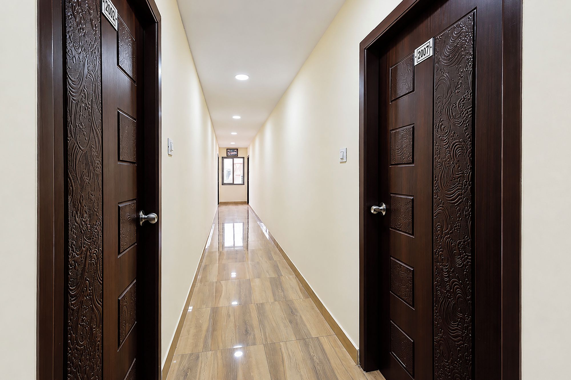 Un pasillo con dos puertas de madera oscura, cada una con una placa de número. El piso está cubierto de baldosas y las paredes están pintadas en un tono claro.