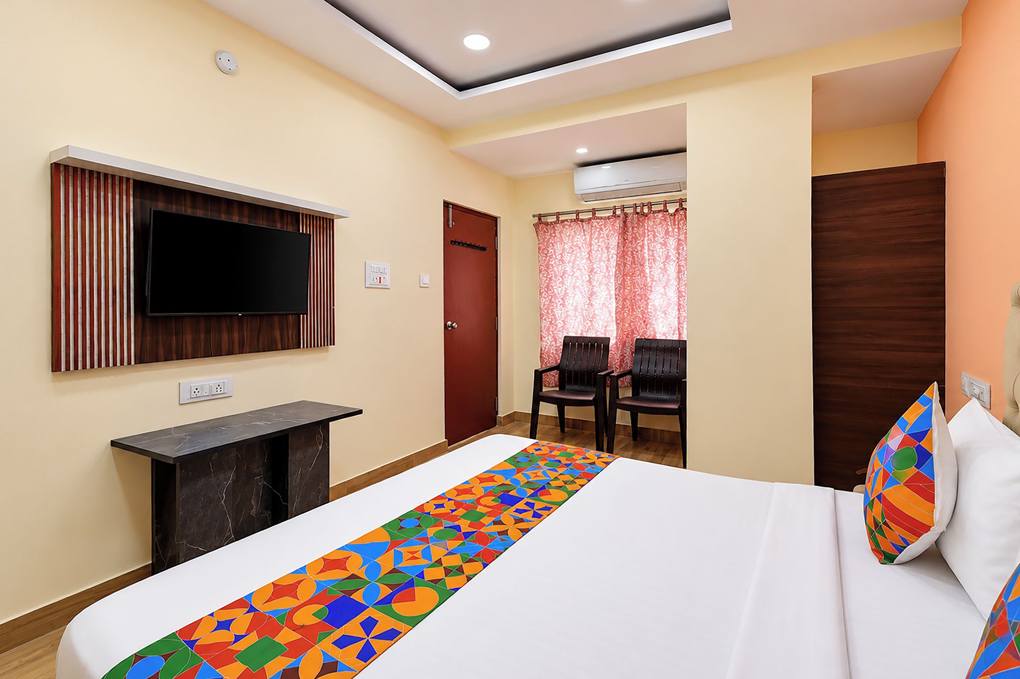 Una habitación de hotel con una cama, un televisor en la pared, un escritorio, una silla y una ventana con cortinas.