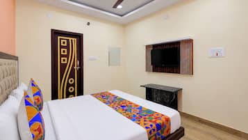 Una habitación de hotel con una cama, un ventilador de techo, un televisor montado en la pared y un escritorio pequeño.
