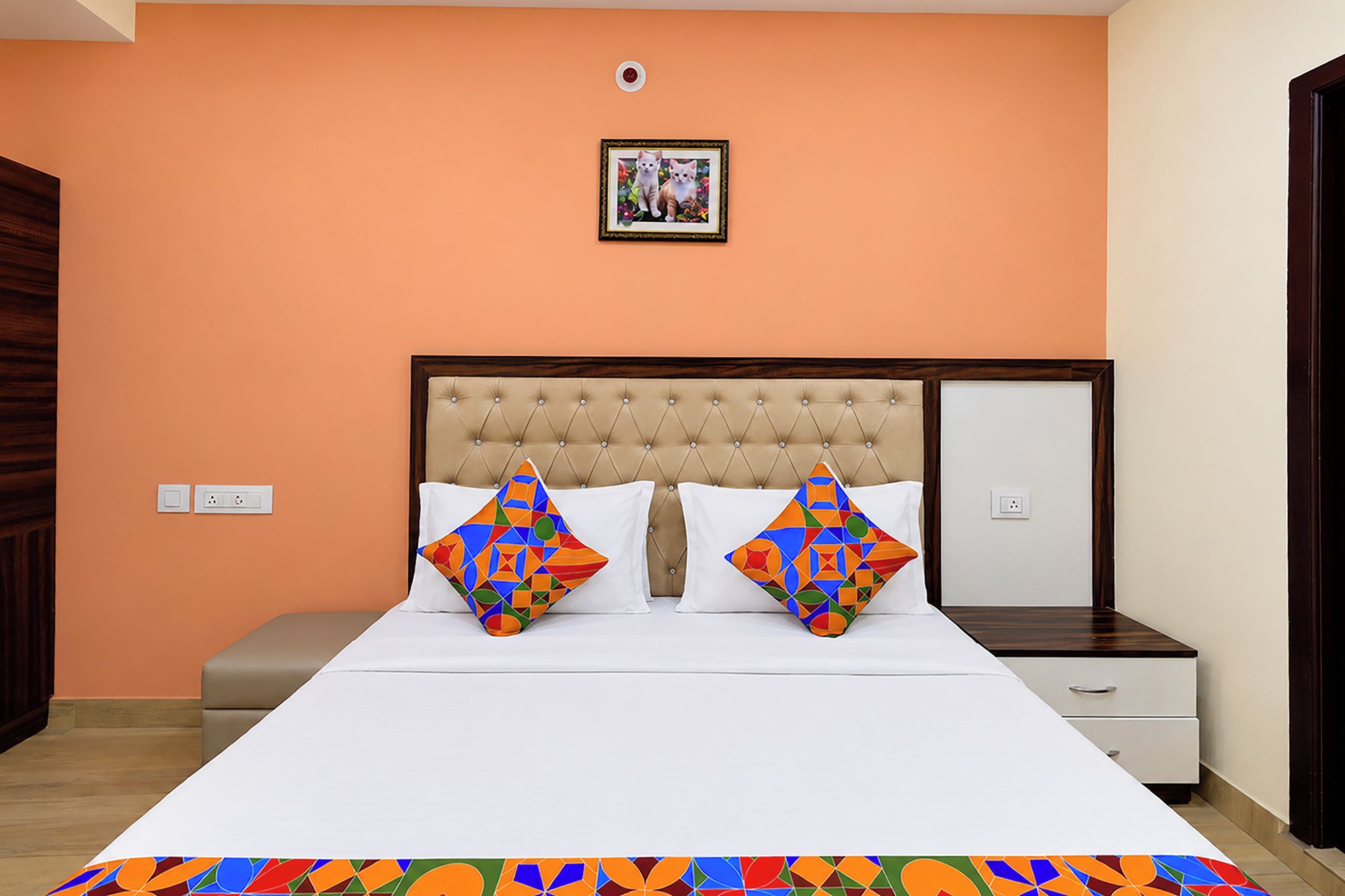 Un dormitorio con una cama, dos almohadas, una mesita de noche, un aparador y un cuadro en la pared.