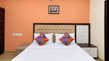 Un dormitorio con una cama, dos almohadas, una mesita de noche, un aparador y un cuadro en la pared.