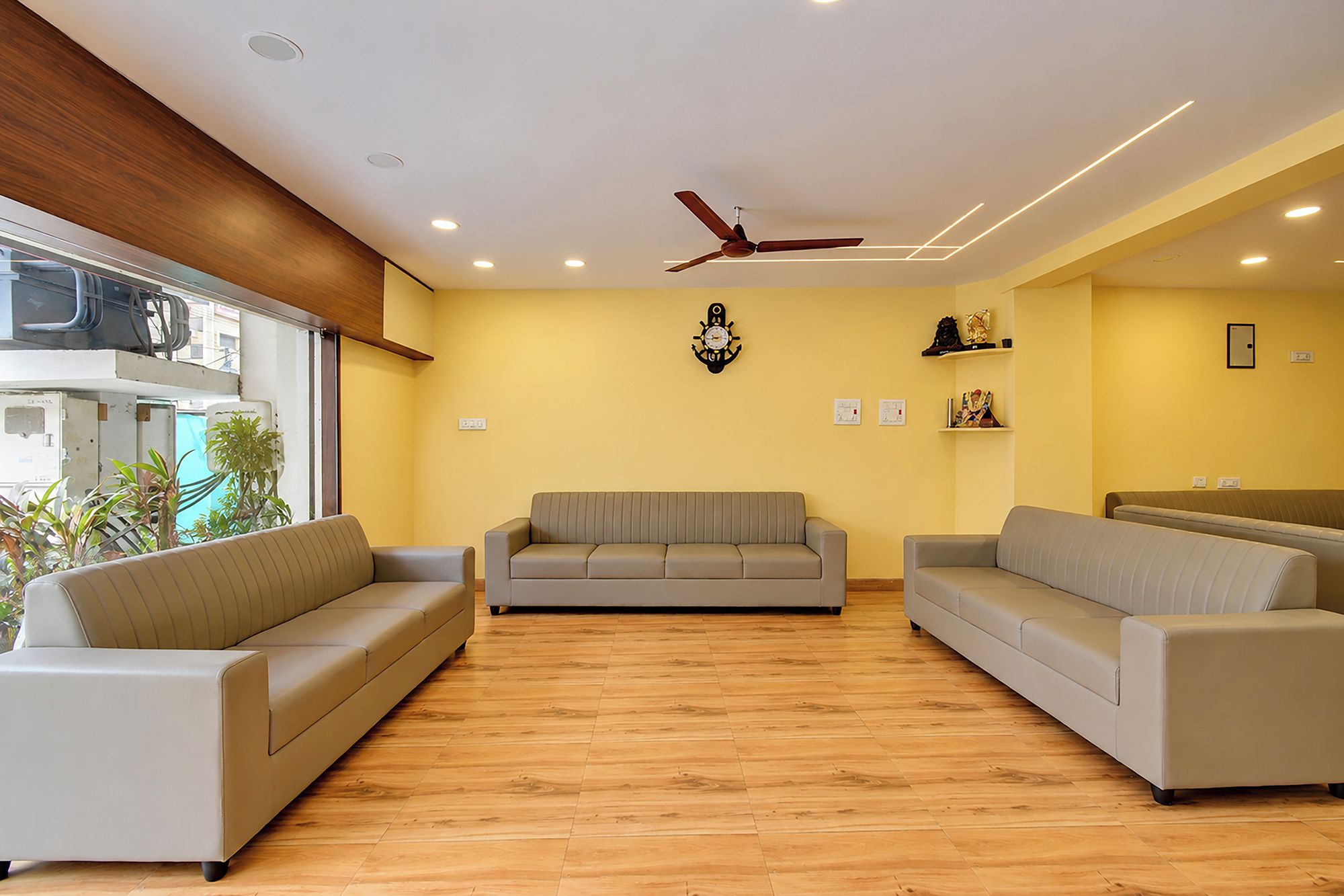 Un amplio salón con suelo de madera, dos sofás, un ventilador de techo y un reloj de pared.