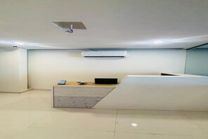 A reception desk with a laptop, a mobile phone, and a small digital device. There is an air conditioning unit mounted on the wall above the desk. - Fabhotel Royal Elite Luxury (Hyderabad)