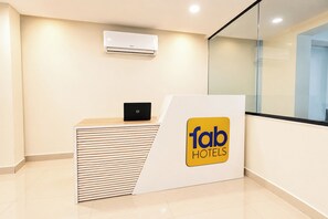 Un comptoir d’accueil avec un ordinateur portable, une enseigne indiquant « fab hotels », et un appareil de climatisation fixé au mur.
