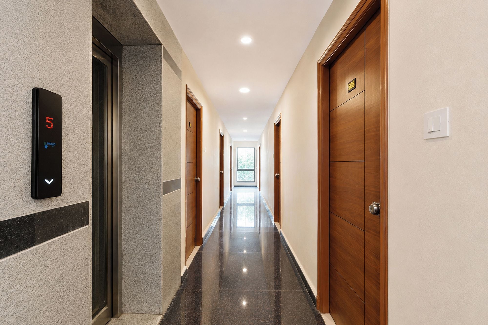 A hotel hallway with a digital elevator display, wooden doors, and a tiled floor.