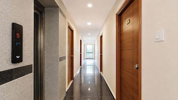 A hotel hallway with a digital elevator display, wooden doors, and a tiled floor.