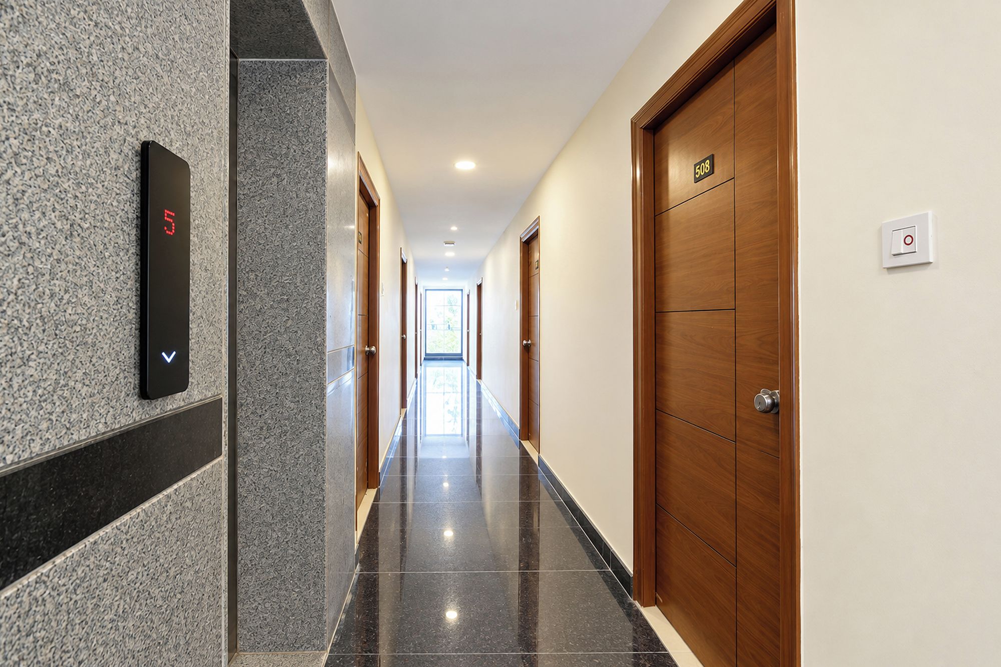 A hotel hallway with a digital elevator display, wooden doors, and a tiled floor.
