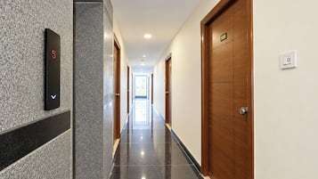 A hotel hallway with a digital elevator display, wooden doors, and a tiled floor.