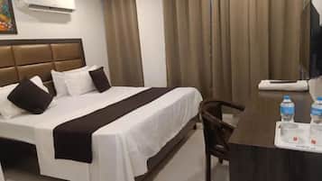 A hotel room with a bed, a desk with a chair, a water bottle, and a mirror.