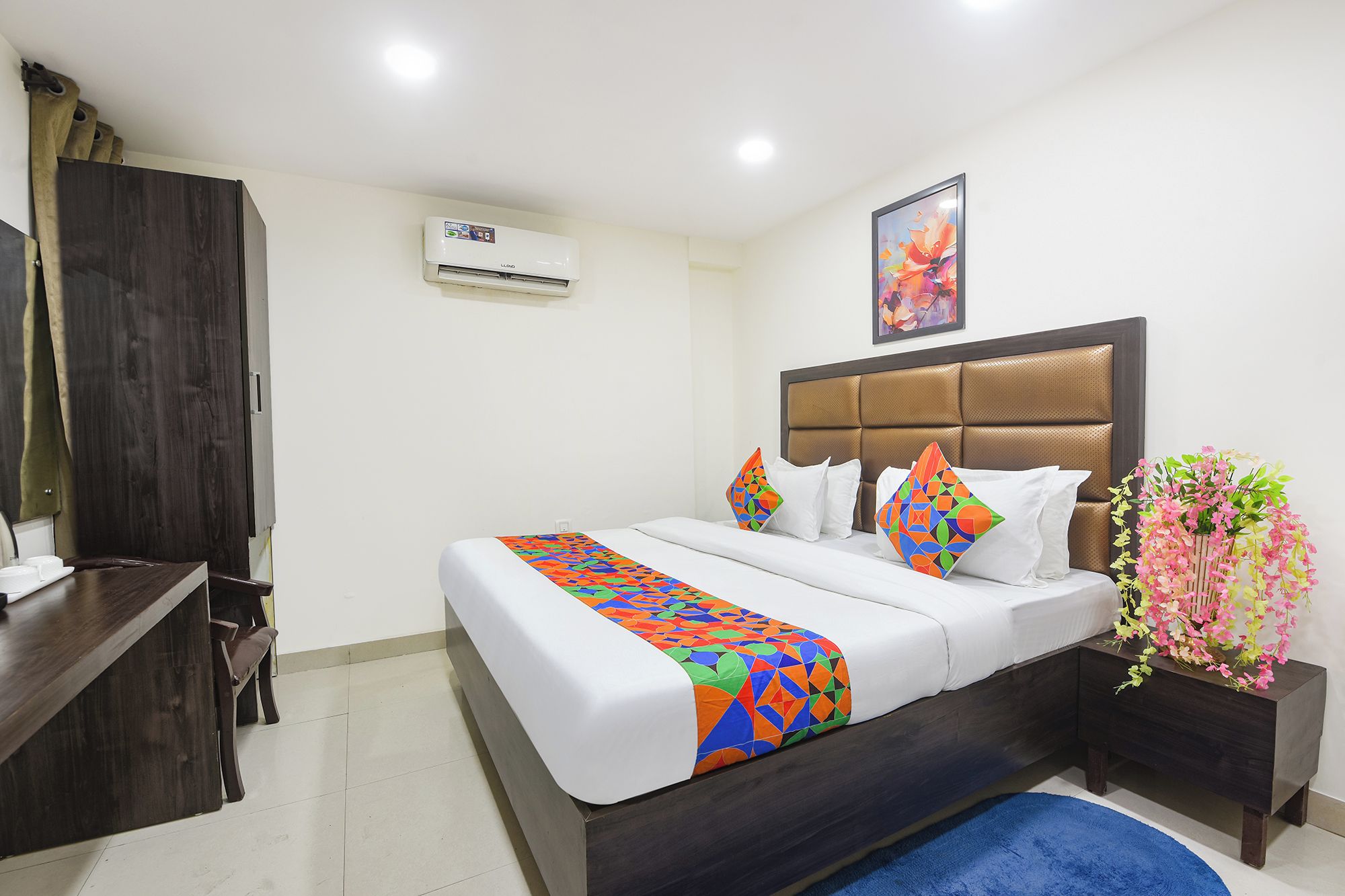 Quarto de hotel com cama, mesa de cabeceira, cômoda, ar condicionado e um quadro na parede.