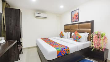 A hotel room with a bed, a nightstand, a dresser, an air conditioning unit, and a painting on the wall.