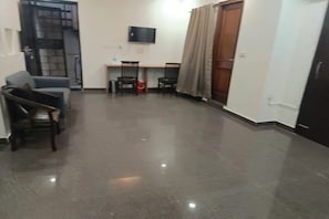 A spacious living area with a polished floor, a sofa, a coffee table, and a TV mounted on the wall. - Fabhotel Sbs Palza (New Delhi)