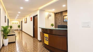 Uma área de recepção de hotel com balcão, piso estampado e plantas em vasos.