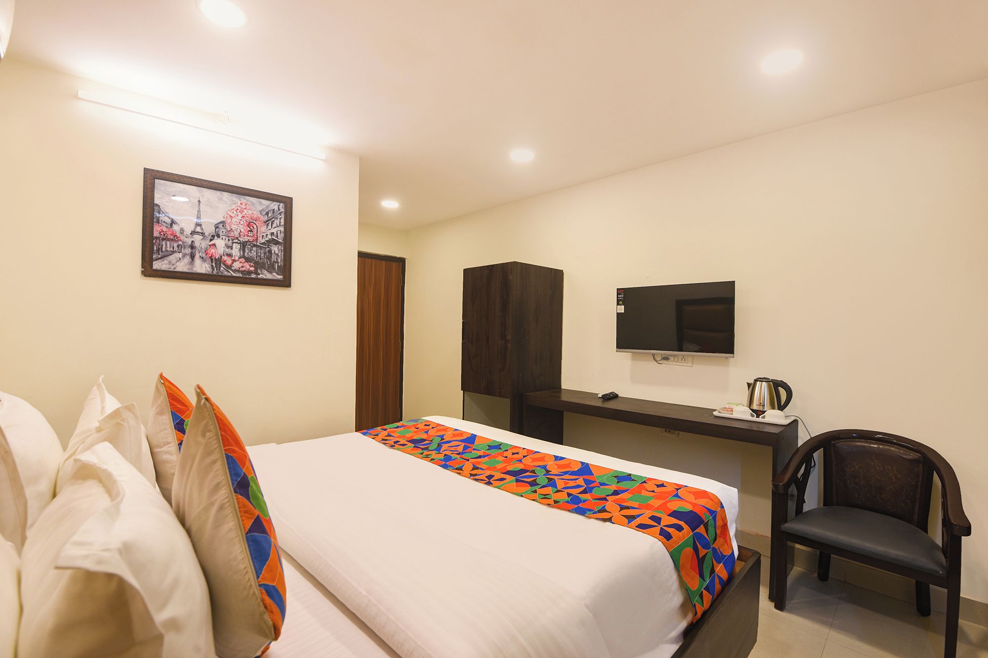 A hotel room with a bed, a desk, a chair, a television, and a picture on the wall.