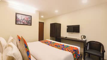 Una habitación de hotel con cama, escritorio, silla, televisión y un cuadro en la pared.
