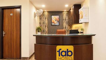 A hotel reception desk with a 'fab hotels' sign, a wooden door, a wall-mounted fan, and a framed artwork.