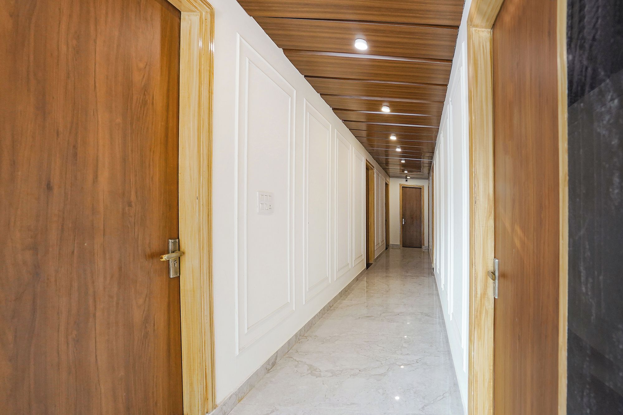 Un pasillo con puertas de madera y piso de mármol, que conduce a una habitación con techo de madera.