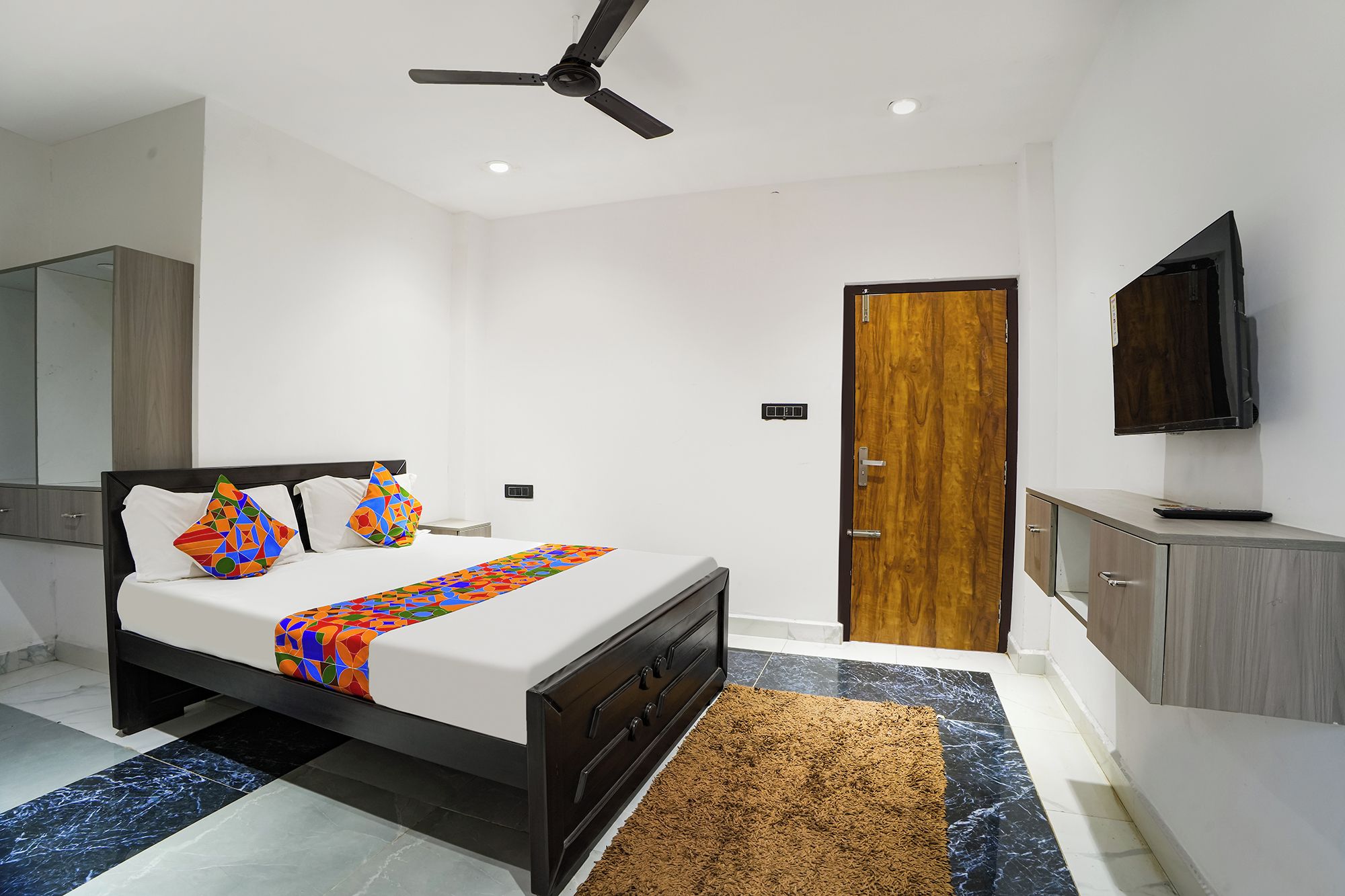 Un dormitorio moderno con una cama, un ventilador de techo, un televisor y una puerta de madera.