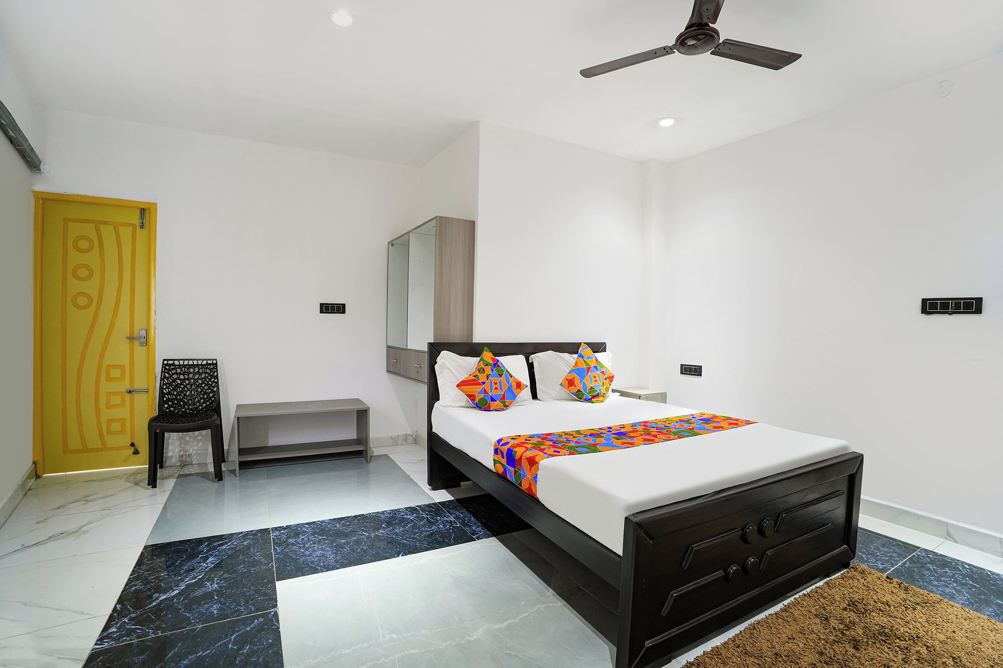 A modern bedroom with a bed, a ceiling fan, a small table, and a yellow door.