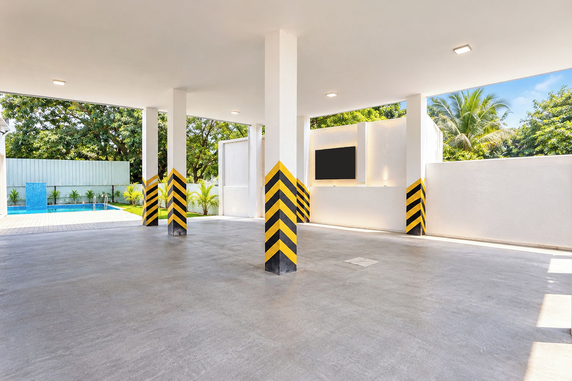 A spacious outdoor area with a pool, white pillars with yellow and black stripes, and a view of greenery.