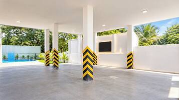 A spacious outdoor area with a pool, white pillars with yellow and black stripes, and a view of greenery.