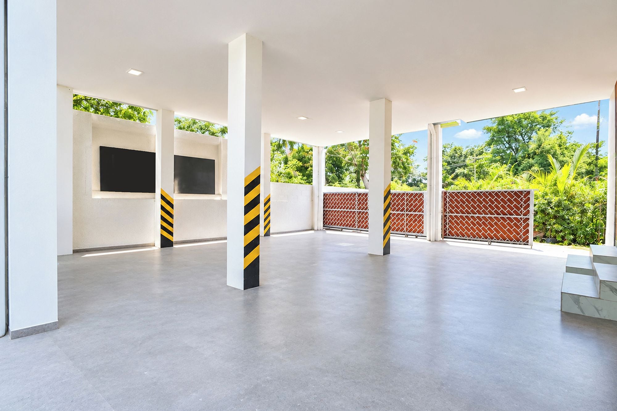 Un espacio interior amplio con techo alto, suelo de hormigón y un gran ventanal con vistas a la vegetación.
