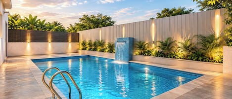 Una piscina rectangular con caída de agua, rodeada por un solárium con baldosas y un muro bajo con paneles verticales.