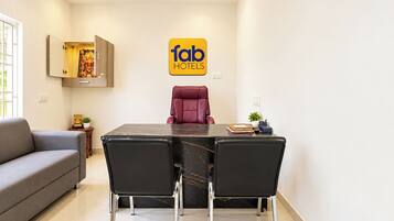 A modern hotel room with a dining table, two chairs, a sofa, and a wall-mounted cabinet.