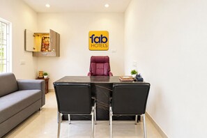 A modern hotel room with a dining table, two chairs, a sofa, and a wall-mounted cabinet. - Fabhotel Ad Holidays (Tirupporur)