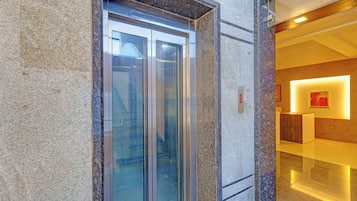 Un ascensor con puertas de vidrio, pared de mármol e interior moderno con una pared de acento rojo y un cuadro enmarcado.