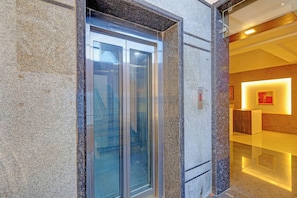 An elevator with glass doors, a marble wall, and a modern interior with a red accent wall and a framed picture.