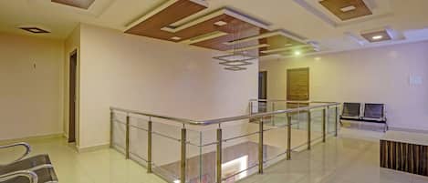 Un interior espacioso con una escalera de barandilla de vidrio, un mostrador de recepción y un diseño de techo moderno.