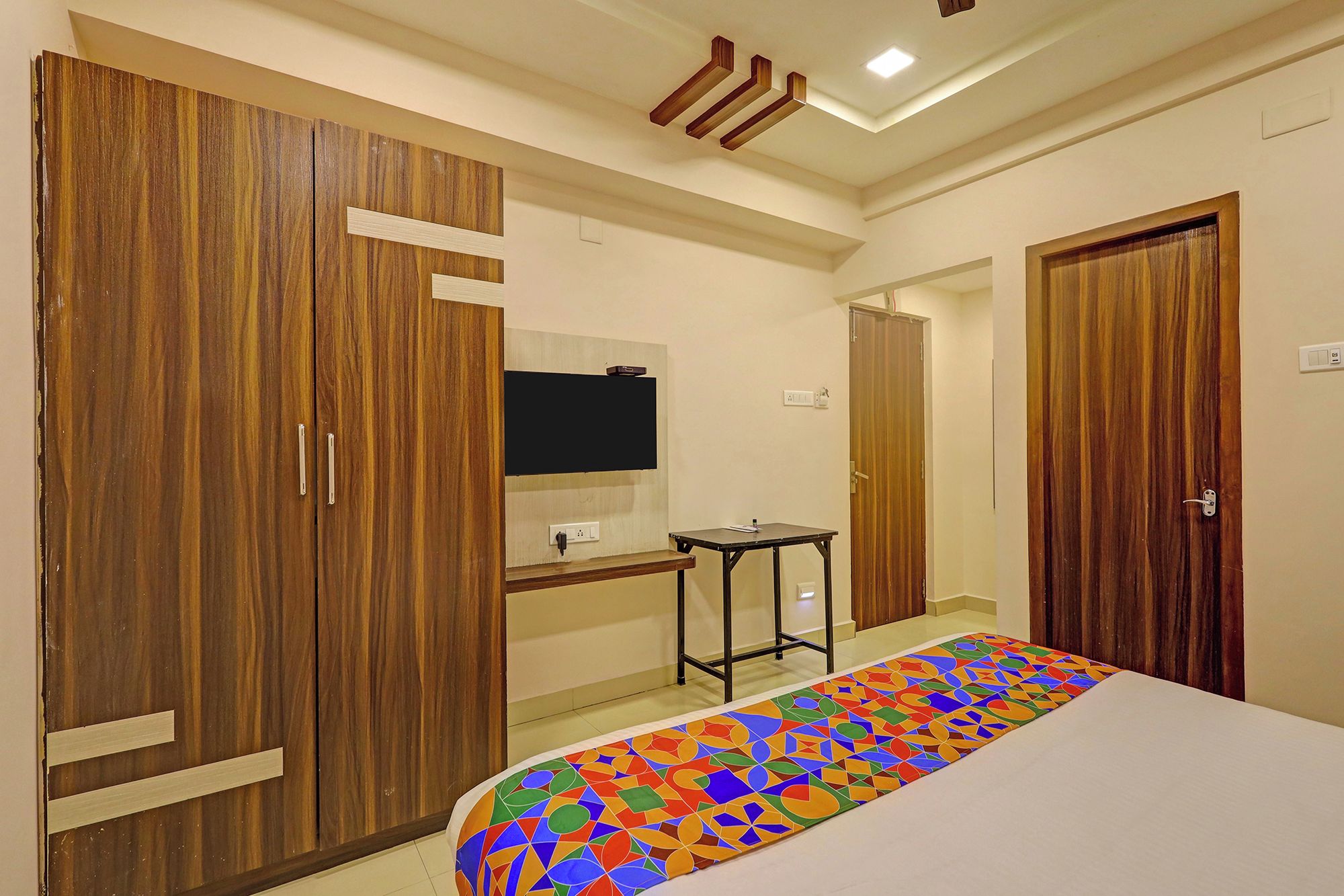 Un dormitorio con cama, armarios de madera, una mesita y televisión instalada en la pared.