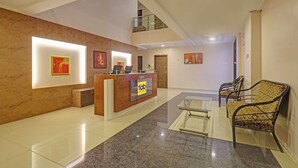 Uma área de recepção de hotel com um balcão de mármore, uma escadaria e uma área de estar com cadeiras estampadas.