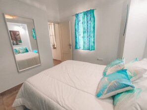 Ein Schlafzimmer mit Bett, Spiegel, einem fenster mit Vorhängen und einer Tür zu einem anderen Raum.