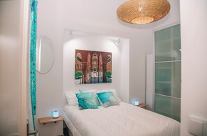 Ein Schlafzimmer mit einem Bett, einem Bild von einem Innenhof, einer Hängelampe und einem Nachttisch mit Lampe.