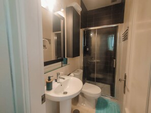 Ein modernes Badezimmer mit einem weißen Waschbecken, einer Toilette und einer Duschkabine aus Glas.