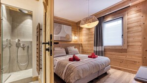 Un dormitorio moderno con detalles de madera, una cama grande con almohadones decorativos, una mesita de noche y un rincón con ducha.